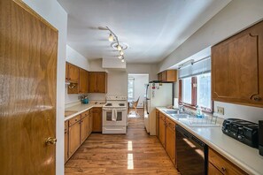 A kitchen with wooden cabinets, a stove, a refrigerator, and a window with blinds. - The Shamrock — 5BR Leadville Home, Game Room + 2-Car Garage, Sleeps 10 (Leadville)