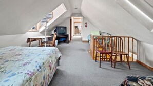 A room with a bed, a desk, a chair, a television, and a staircase. - The Painted Lady — Victorian 4BR Steps to Main St Leadville, Sleeps 10, Dogs OK (Leadville)