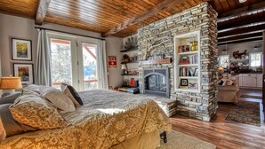 A cozy bedroom with a stone fireplace, a large bed with patterned bedding, and a view of the outside. - Mountain-View Cabin w/ Fireplace & Deck (Twin Lakes)