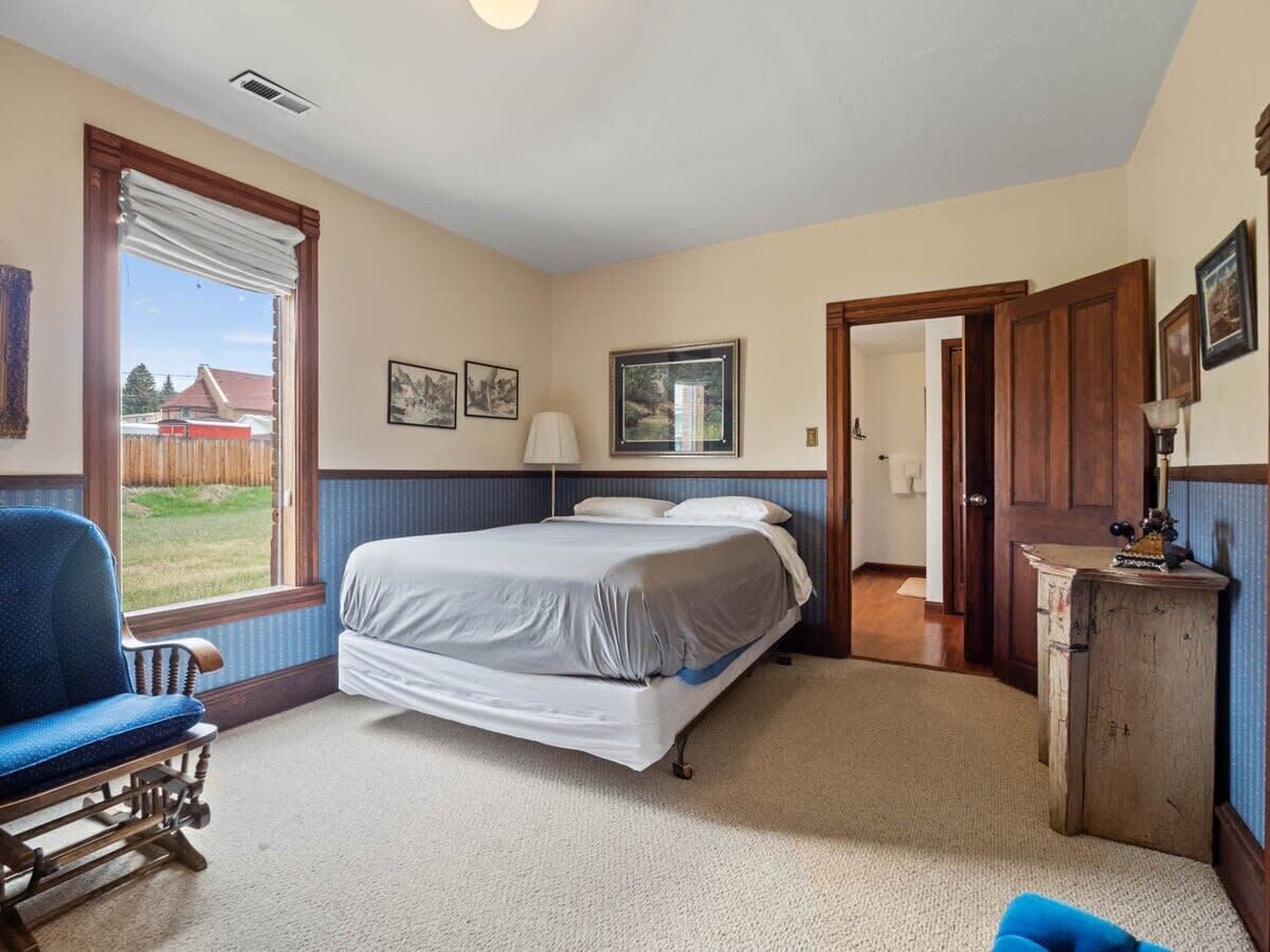 A bedroom with a bed, a chair, a desk, and a window.