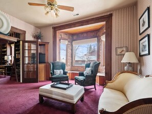 Ein gemütliches Wohnzimmer mit Kamin, einer Couch, zwei Sesseln, einem Couchtisch und einem Bücherregal.