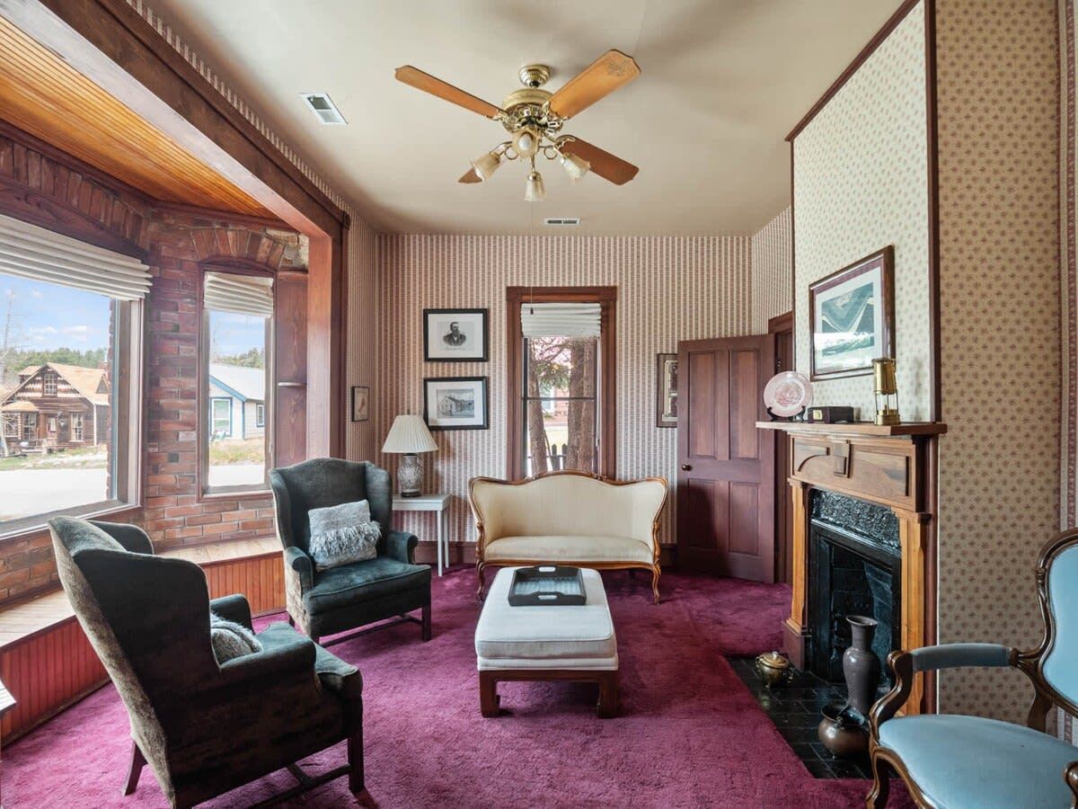 A room with a fireplace, a ceiling fan, and a large window with blinds.