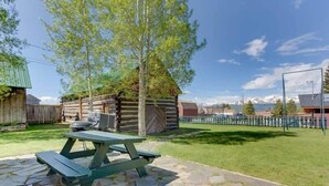 A rustic outdoor setting with a stone patio, a picnic table, and a wooden cabin. - Historic 3BR w/ Loft:Mountain View & Near Town (Leadville)