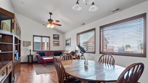 A spacious room with a wooden dining table, chairs, a sofa, a ceiling fan, and large windows. - Historic 3BR w/ Loft:Mountain View & Near Town (Leadville)