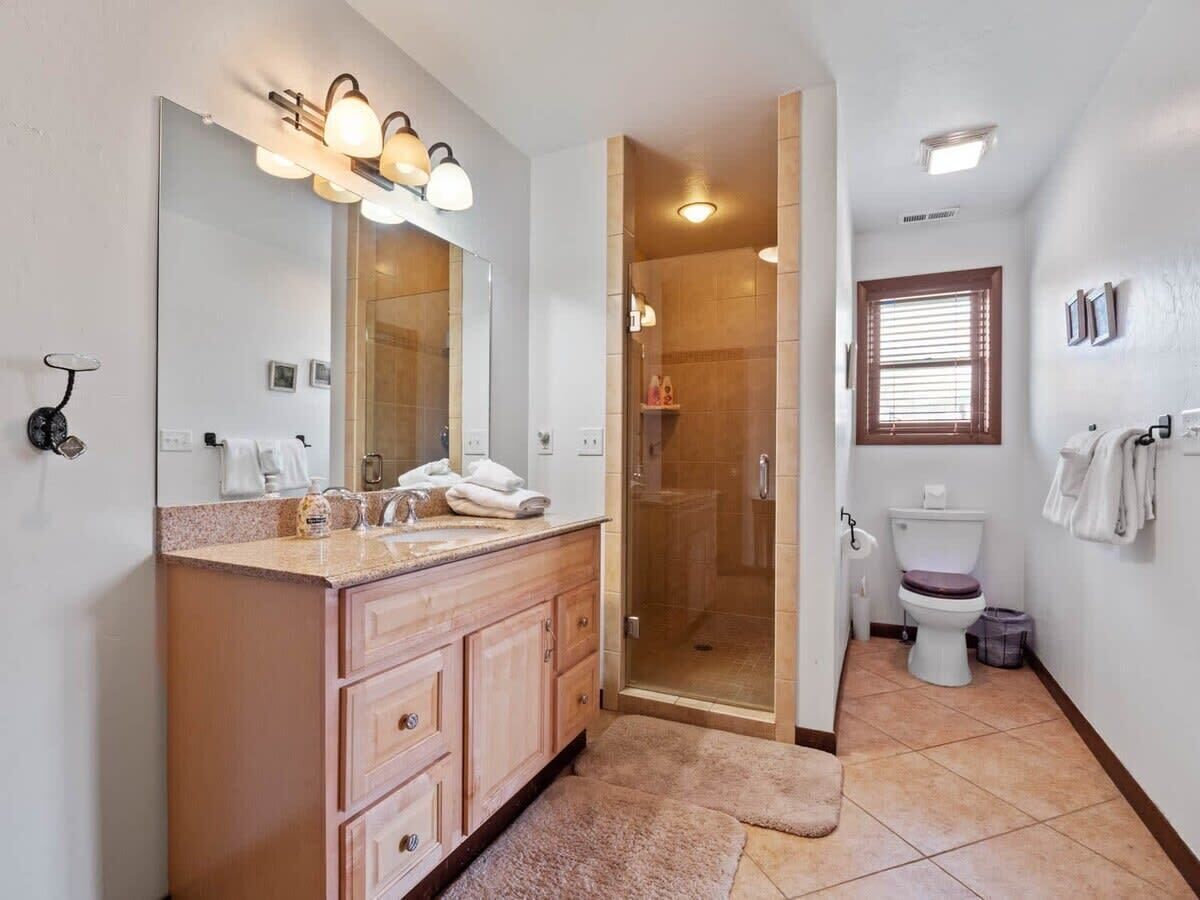 A bathroom with a large mirror, a shower, a toilet, and a sink.
