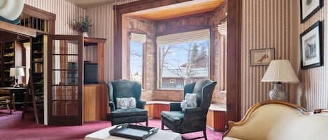 A cozy living room with a fireplace, a sofa, two armchairs, a coffee table, and a bookshelf.