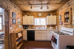 A rustic wooden cabin interior with a kitchen featuring white cabinets, a stove, a dishwasher, and a window. - The Rosemont — Historic 4BR Leadville Victorian, Loft, Fireplace, 2 Blocks Down (Leadville)