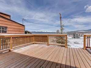 Una terraza de madera con barandilla, vista a montañas nevadas y cielo despejado.