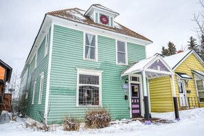 A green house with a porch, a chimney, and a small attached garage. - The Rosemont — Historic 4BR Leadville Victorian, Loft, Fireplace, 2 Blocks Down (Leadville)