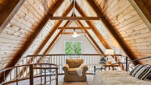 Ein gemütliches Schlafzimmer im Dachgeschoss mit schrägem Dach, einem Bett, einem Sessel und einem kleinen Tisch mit einer Lampe.