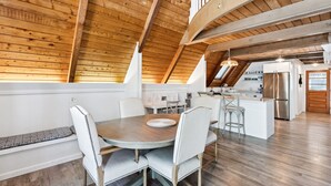 Ein Essbereich mit einem runden Tisch und weiß gepolsterten Stühlen, eine Küche mit Edelstahlgeräten sowie eine Holzbalkendecke.