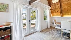 Ein Zimmer mit Holzboden, weißen Wänden, einem Esstisch mit Stühlen und einem großen Fenster mit Vorhängen.