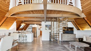 Ein geräumiges Loft mit hoher Decke, Holzbalken, einer zentralen Treppe und einer Küchenzeile.