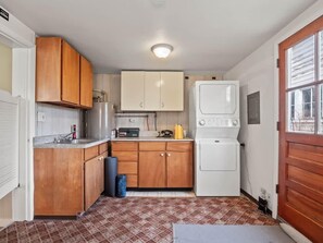 Una cocina compacta con armarios de madera, lavadora integrada y suelo de baldosas.