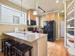 A kitchen with a central island, bar stools, a black refrigerator, wooden cabinets, a microwave, and a window with blinds. - Historic 2BR Home, Downtown Leadville, Mountain Vi (Leadville)