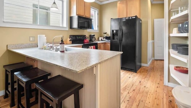 A kitchen with a central island, wooden bar stools, a black refrigerator, and wooden cabinets. - Historic 2BR Home, Downtown Leadville, Mountain Vi (Leadville)
