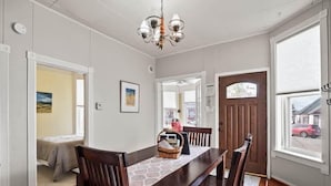A dining area with a wooden table and chairs, a chandelier, and a view of the street through a large window. - Historic 2BR Home, Downtown Leadville, Mountain Vi (Leadville)