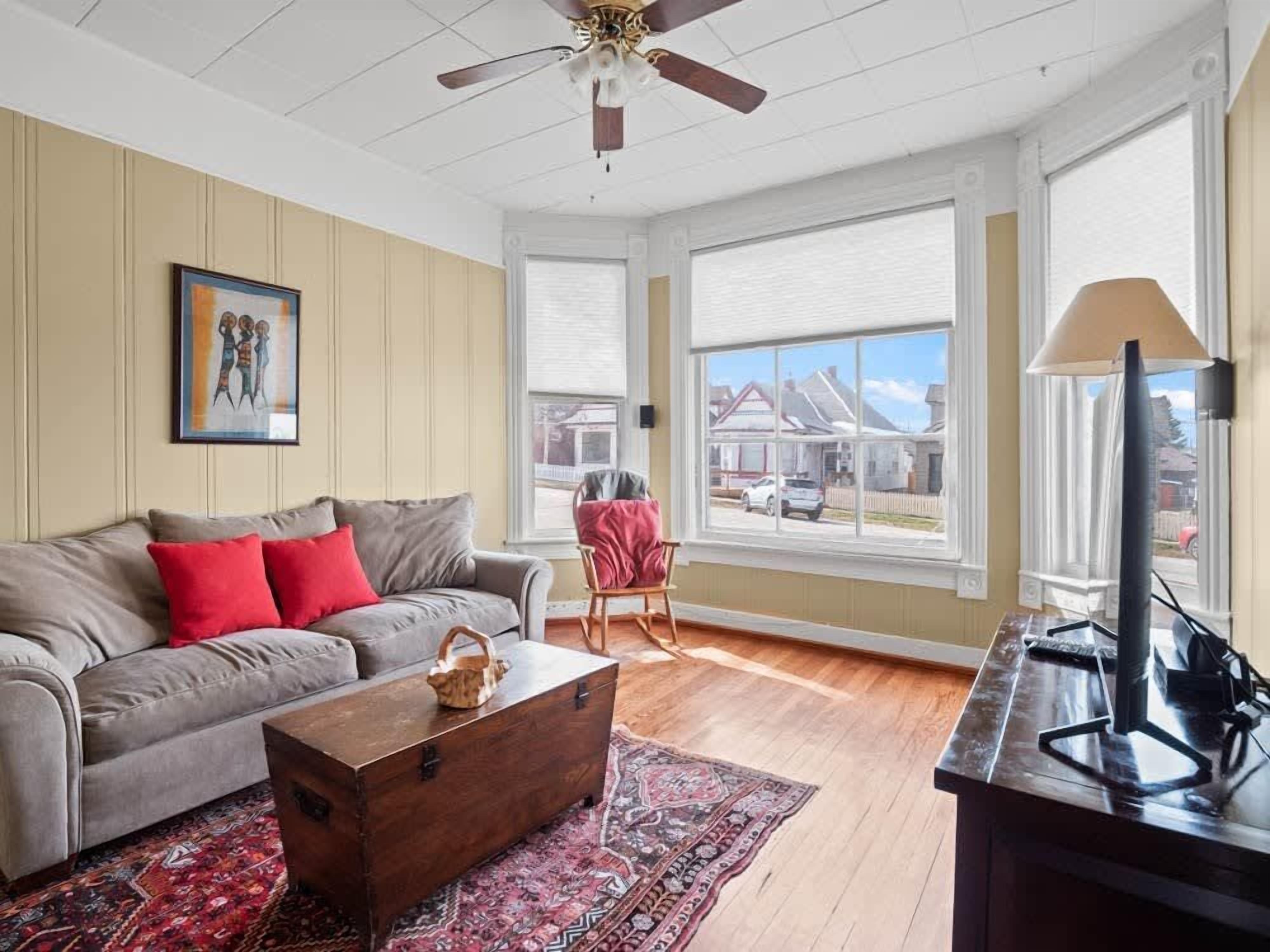 A living room with a sofa, a wooden chest, a rug, a lamp, and a ceiling fan.