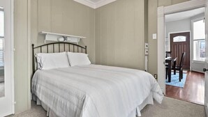 A bedroom with a bed, a nightstand, and a door leading to another room. - Historic 2BR Home, Downtown Leadville, Mountain Vi (Leadville)