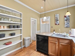 Una cocina compacta con estantes blancos, lavavajillas, armarios de madera y un lavabo.