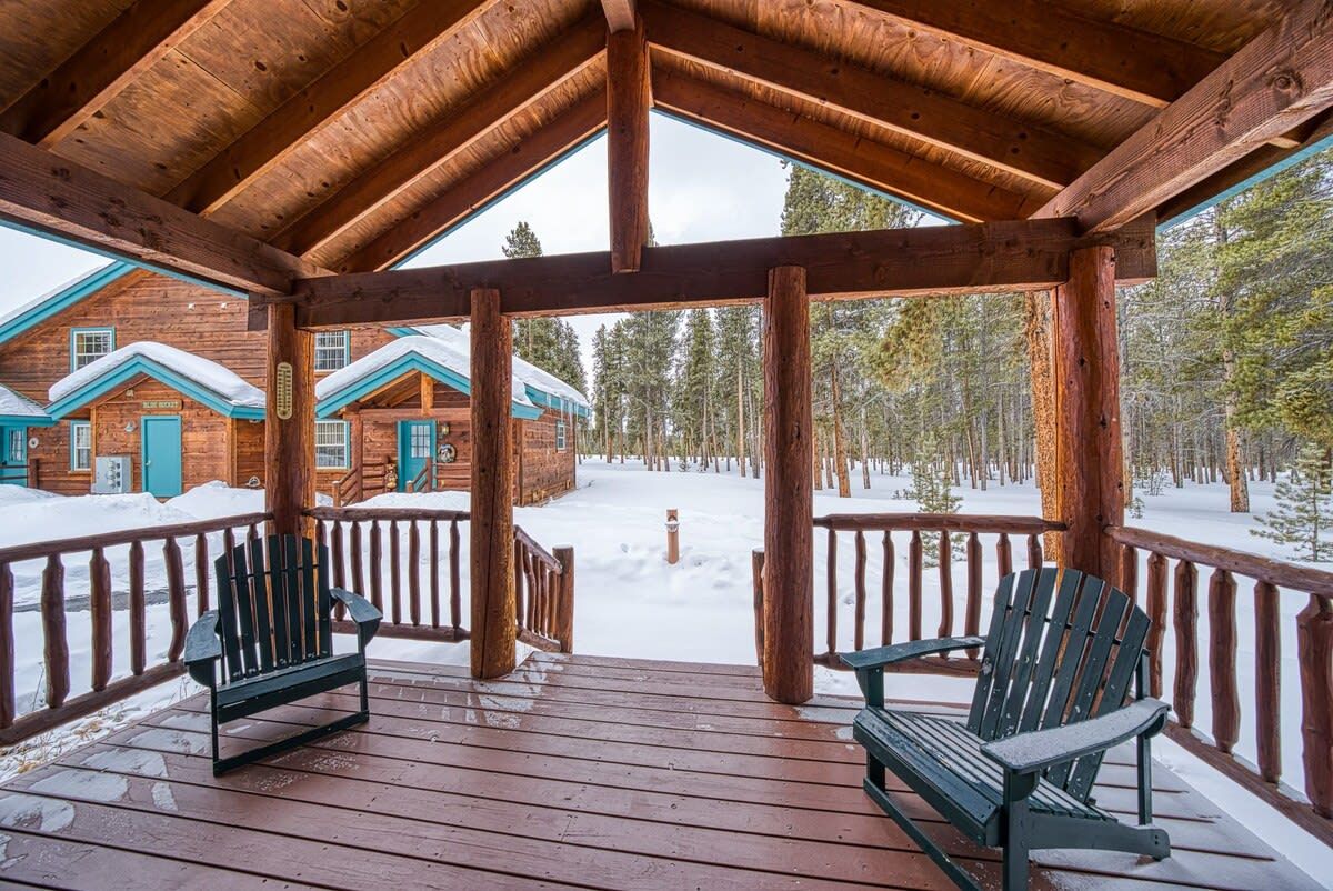A wooden cabin with a covered porch, two Adirondack chairs, and a snowy landscape.