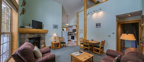 Uma sala de estar acolhedora com lareira, sofás de couro, mesa de centro e área de jantar com mobiliário de madeira.