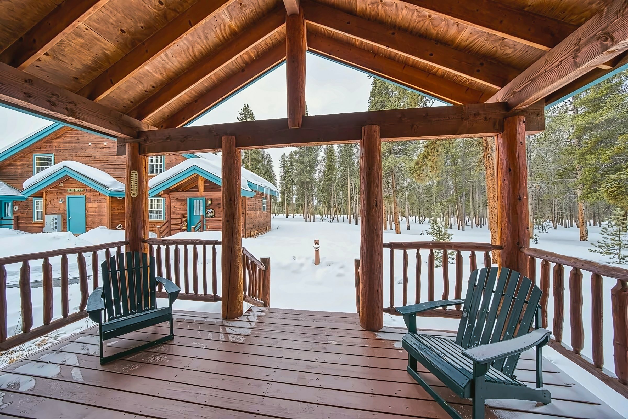 A wooden cabin with a covered porch, two Adirondack chairs, and a snowy landscape.