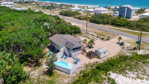 A coastal property with a swimming pool, a large house, and a smaller building, surrounded by lush greenery and a clear view of the ocean. - The Beachy Pool • Cozy SGI Cottage • Pool (St. George island)