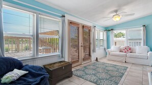 A sunlit room with a blue and white color scheme, featuring a sofa, a chest of drawers, and a ceiling fan. - The Beachy Pool • Cozy SGI Cottage • Pool (St. George island)