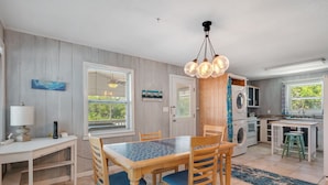 A compact kitchen with a dining area, a washing machine, and a small island with stools. - The Beachy Pool • Cozy SGI Cottage • Pool (St. George island)