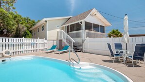 A swimming pool with lounge chairs, a covered deck, and a house with a screened porch. - The Beachy Pool • Cozy SGI Cottage • Pool (St. George island)