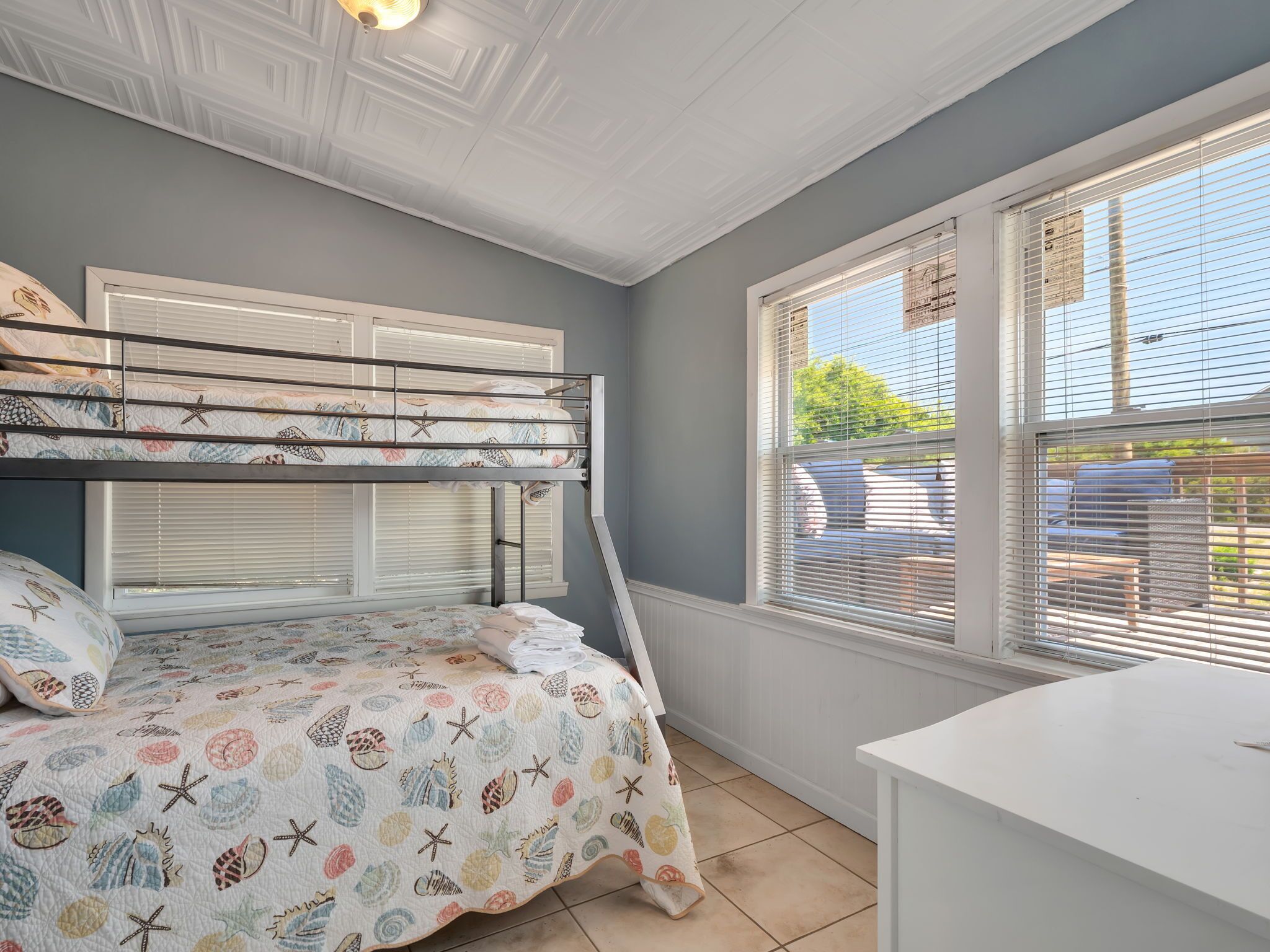 A bedroom with bunk beds, a window with blinds, and a white desk.