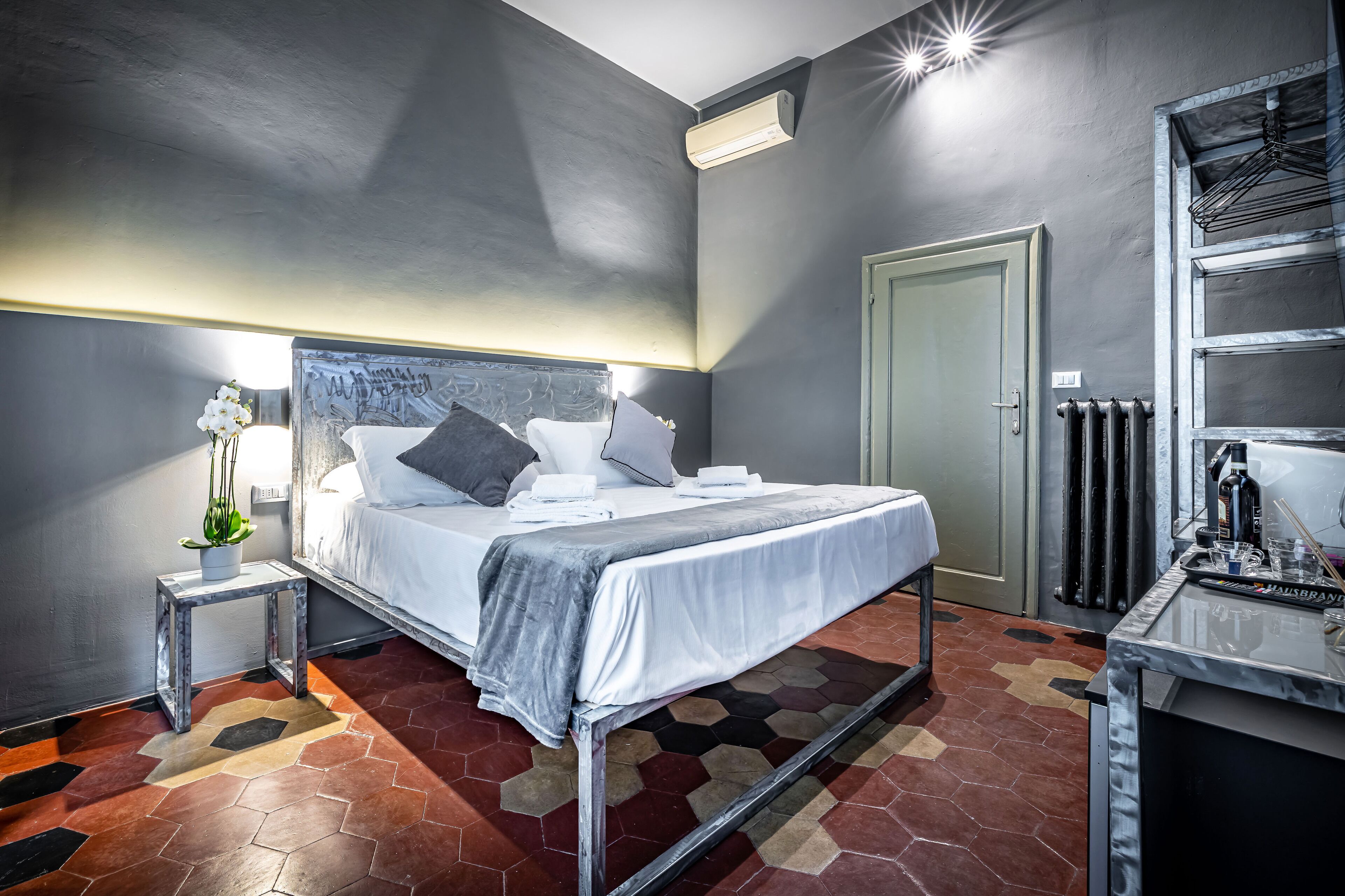 Moderni hotellihuone, jossa on suuri sänky, yöpöytä lampun kanssa, patteri ja vaatekaappi.