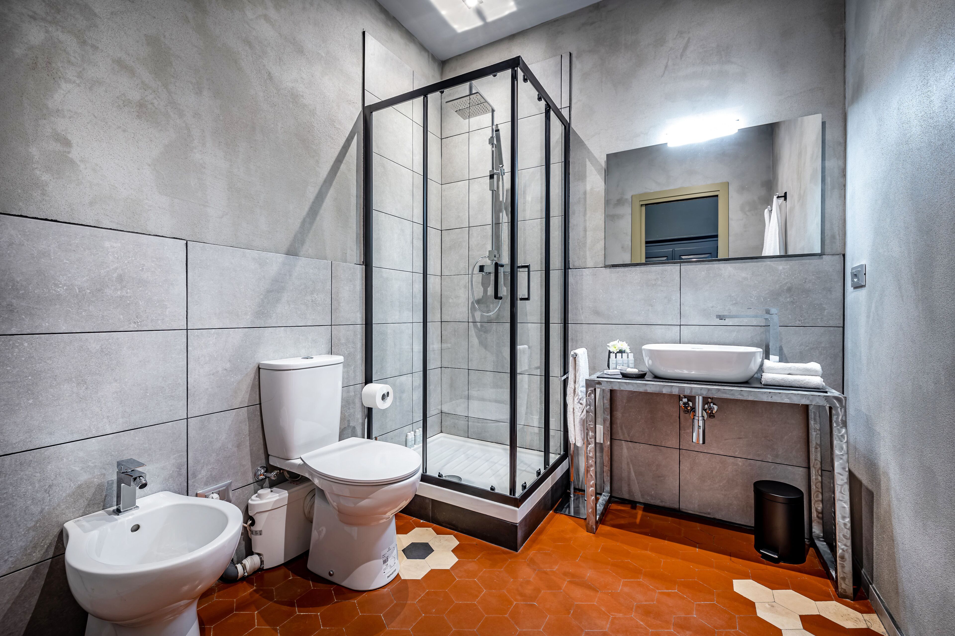 A modern bathroom with a glass-enclosed shower, a bidet, a toilet, and a sink with a mirror above.