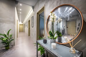 Un couloir doté d’un sol en marbre, d’un grand miroir rond et de plantes en pot.
