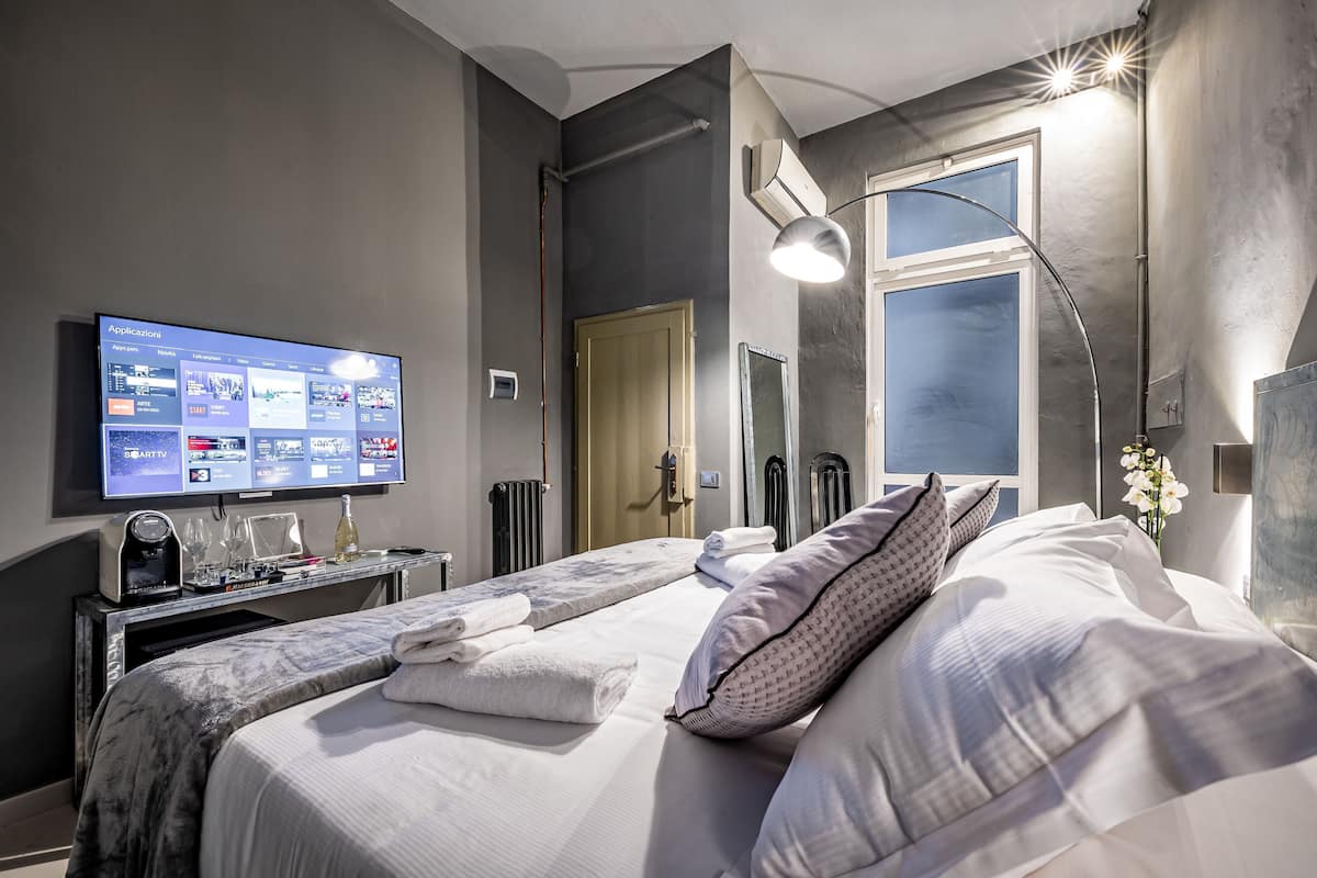 A hotel room with a bed, a TV displaying a room service menu, a desk with a coffee machine, and a window with a view.