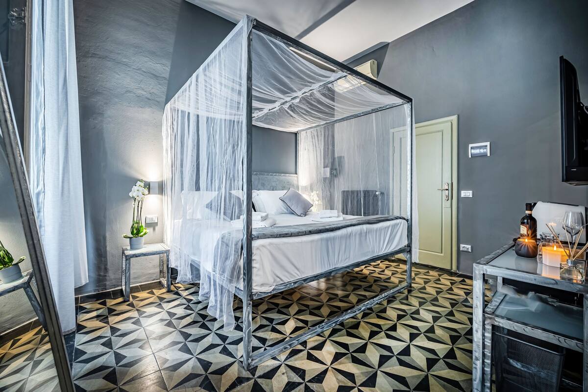 A room with a four-poster bed, a small bedside table with a lamp, and a decorative vase.