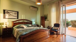 Un dormitorio con cama de madera, mesita de noche, silla, un cuadro en la pared y vistas a través de una puerta corredera.