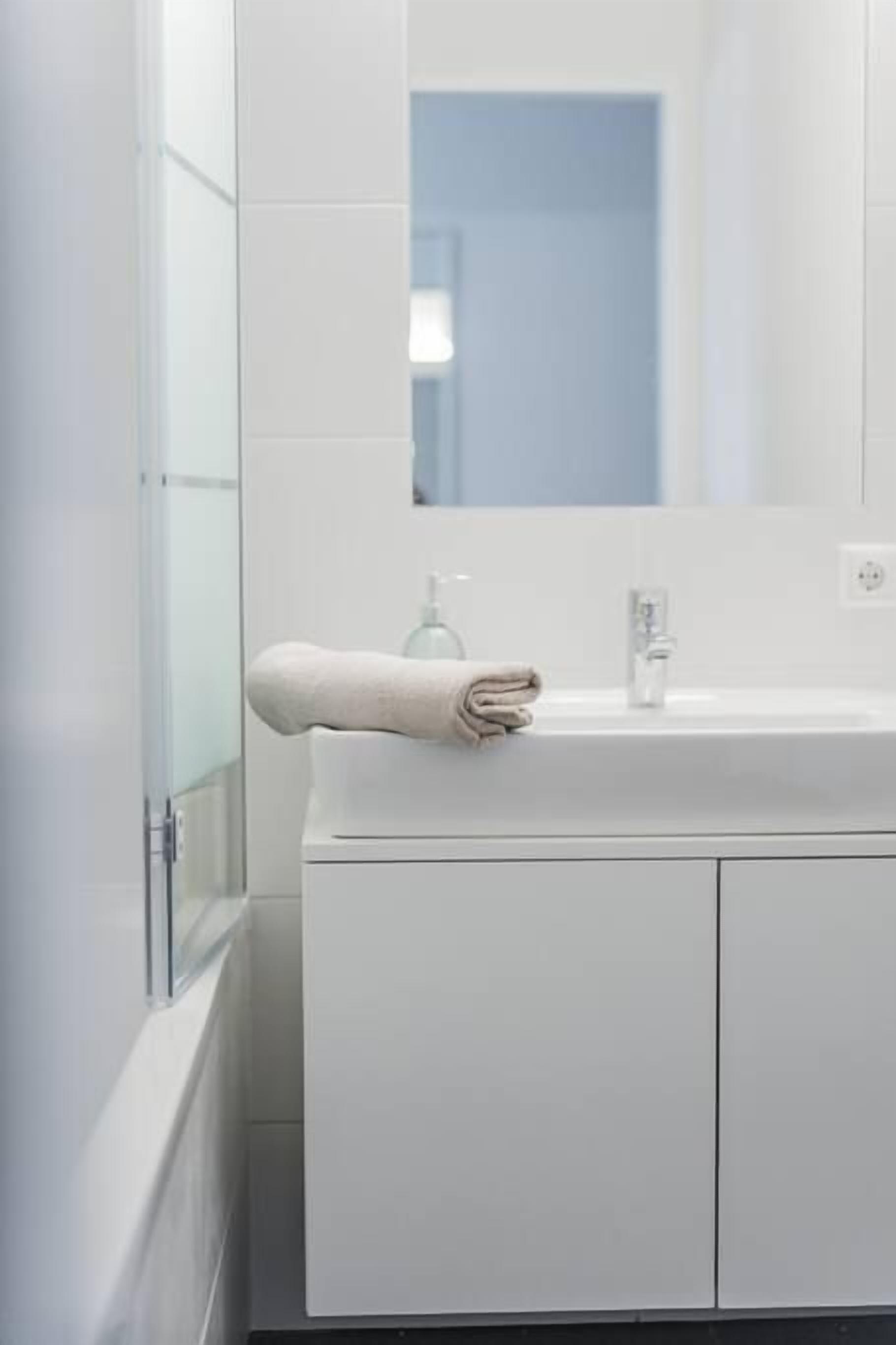 Un baño moderno con un lavabo blanco, un espejo y una toalla colgada en la pared.