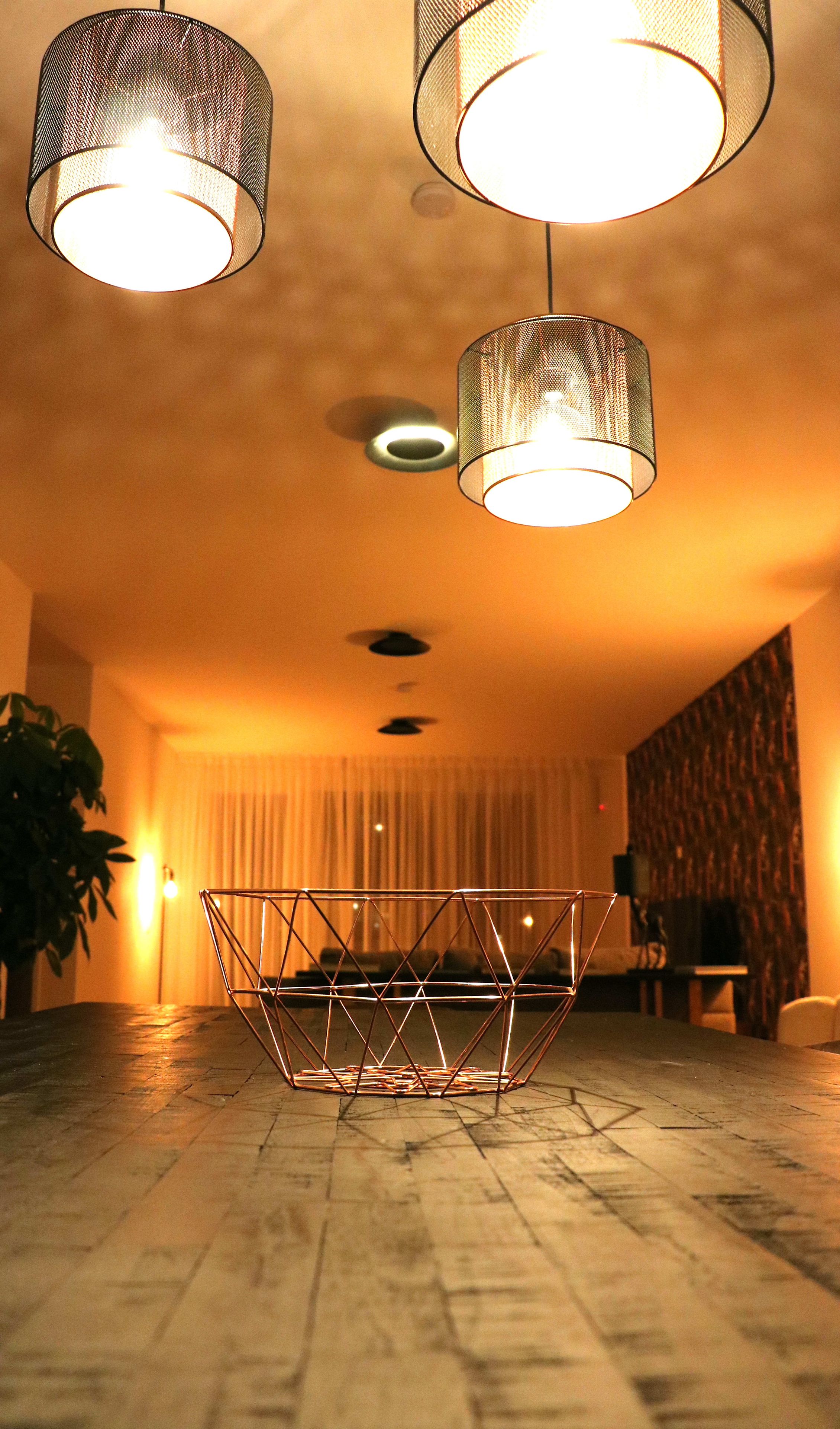 Ein modernes Interieur mit einem geometrischen Metalltisch, zwei hängenden Pendelleuchten und einer warmen, indirekten Beleuchtung.