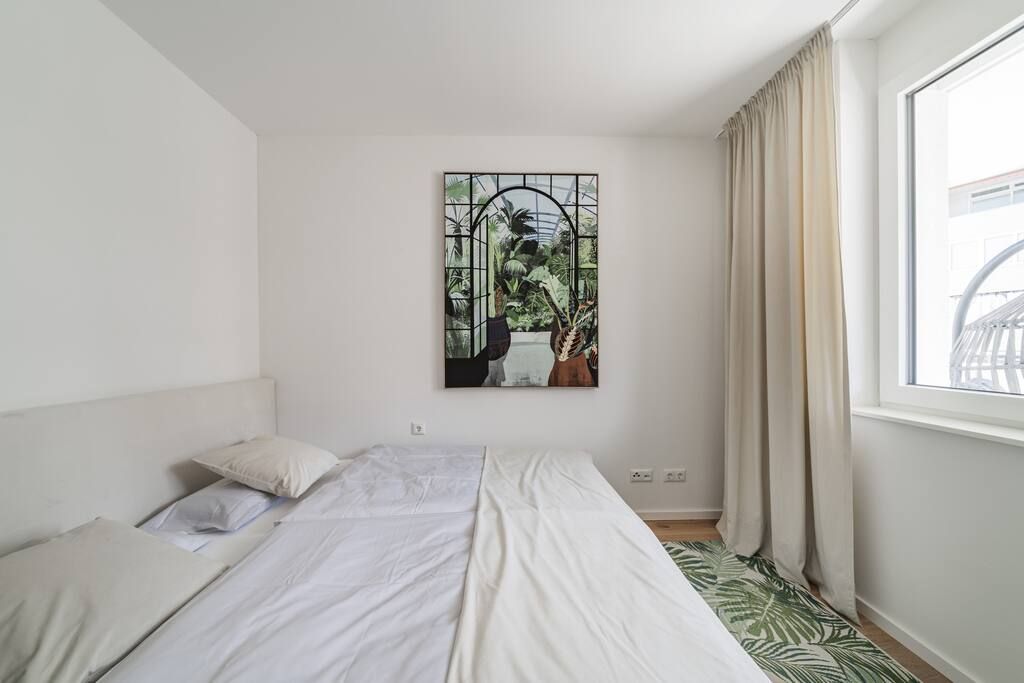 Ein Schlafzimmer mit einem Bett, einem Fenster mit Vorhängen und einem an der Wand hängenden Kunstwerk.