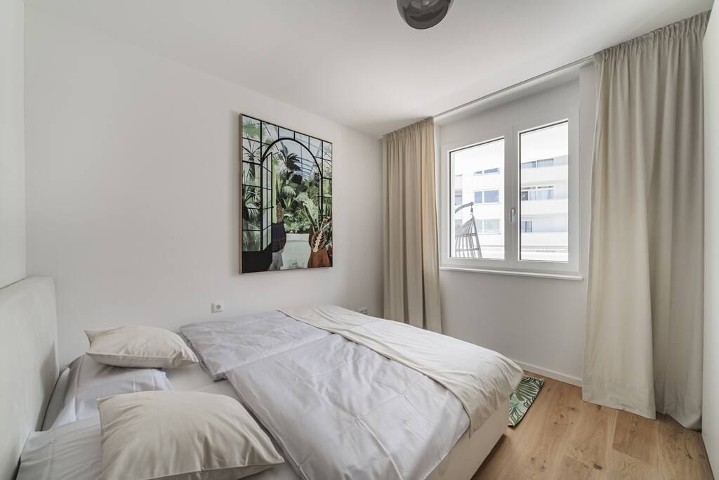 A bedroom with a bed, a window with curtains, and a wall-mounted artwork.
