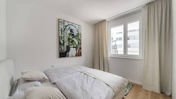 A bedroom with a bed, a window with curtains, and a wall-mounted artwork.