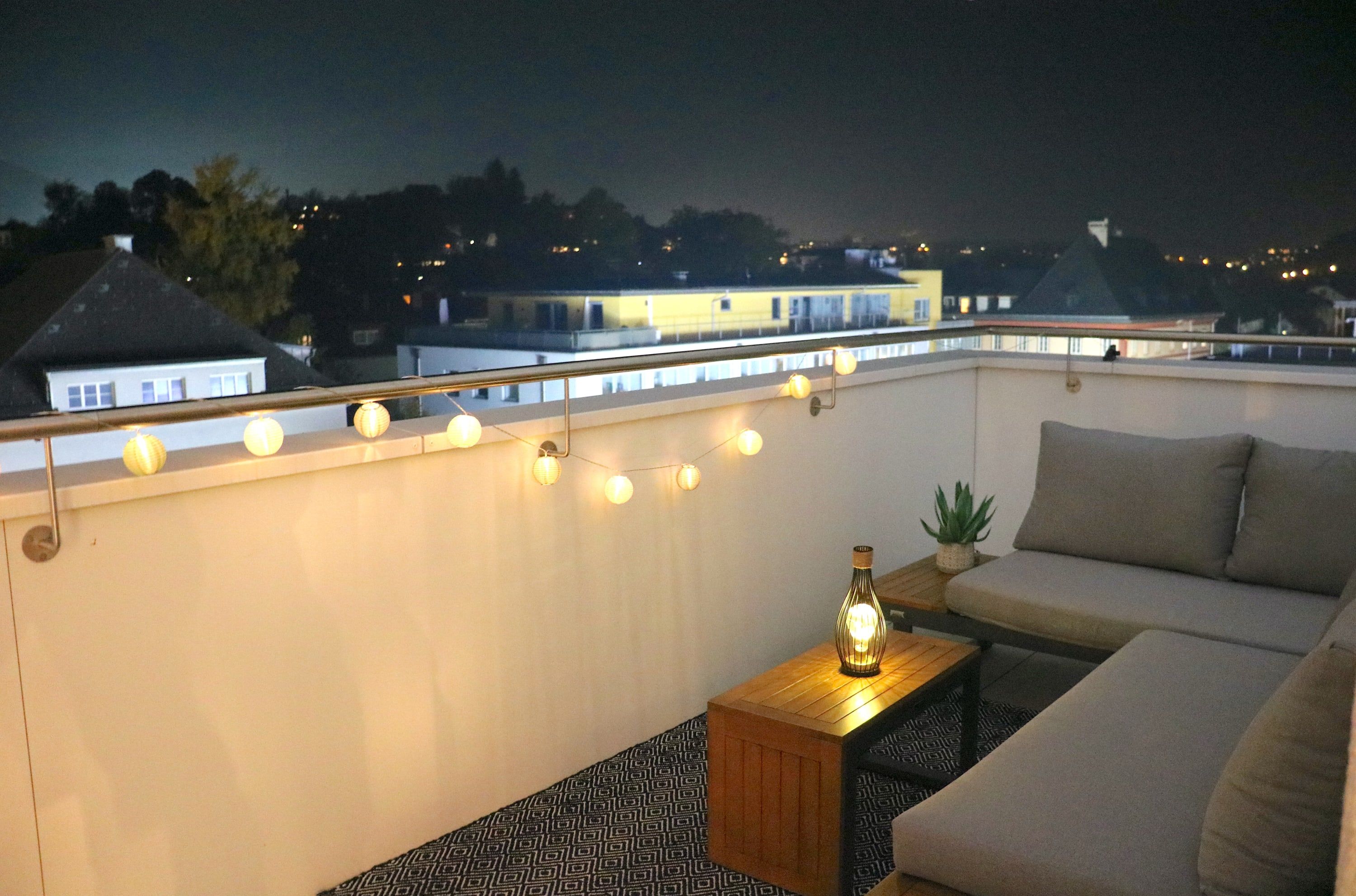 A rooftop terrace with a sofa, a small table with a bottle, and string lights.