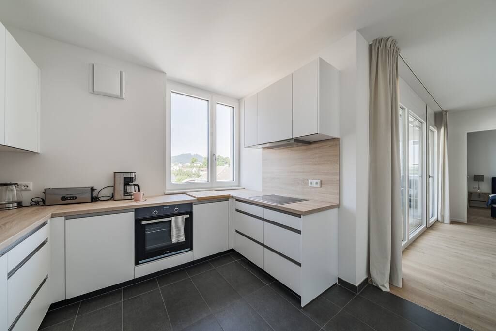 A modern kitchen with white cabinets, a built-in oven, a coffee maker, and a large window.