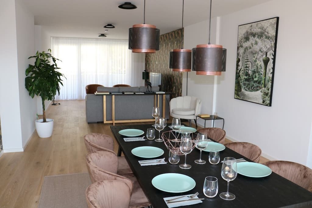 Een moderne eetruimte met een lange tafel gedekt voor zes personen, omringd door fauteuils.