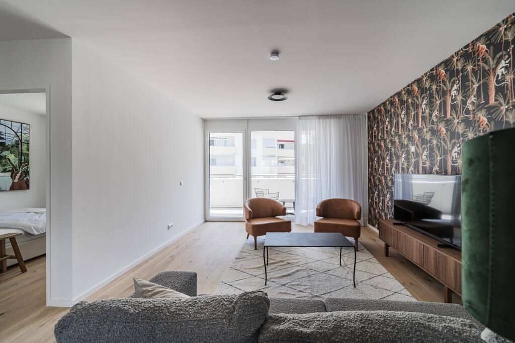 Un salon moderne comprenant un canapé, deux fauteuils, une table basse et un téléviseur posé sur un meuble en bois.