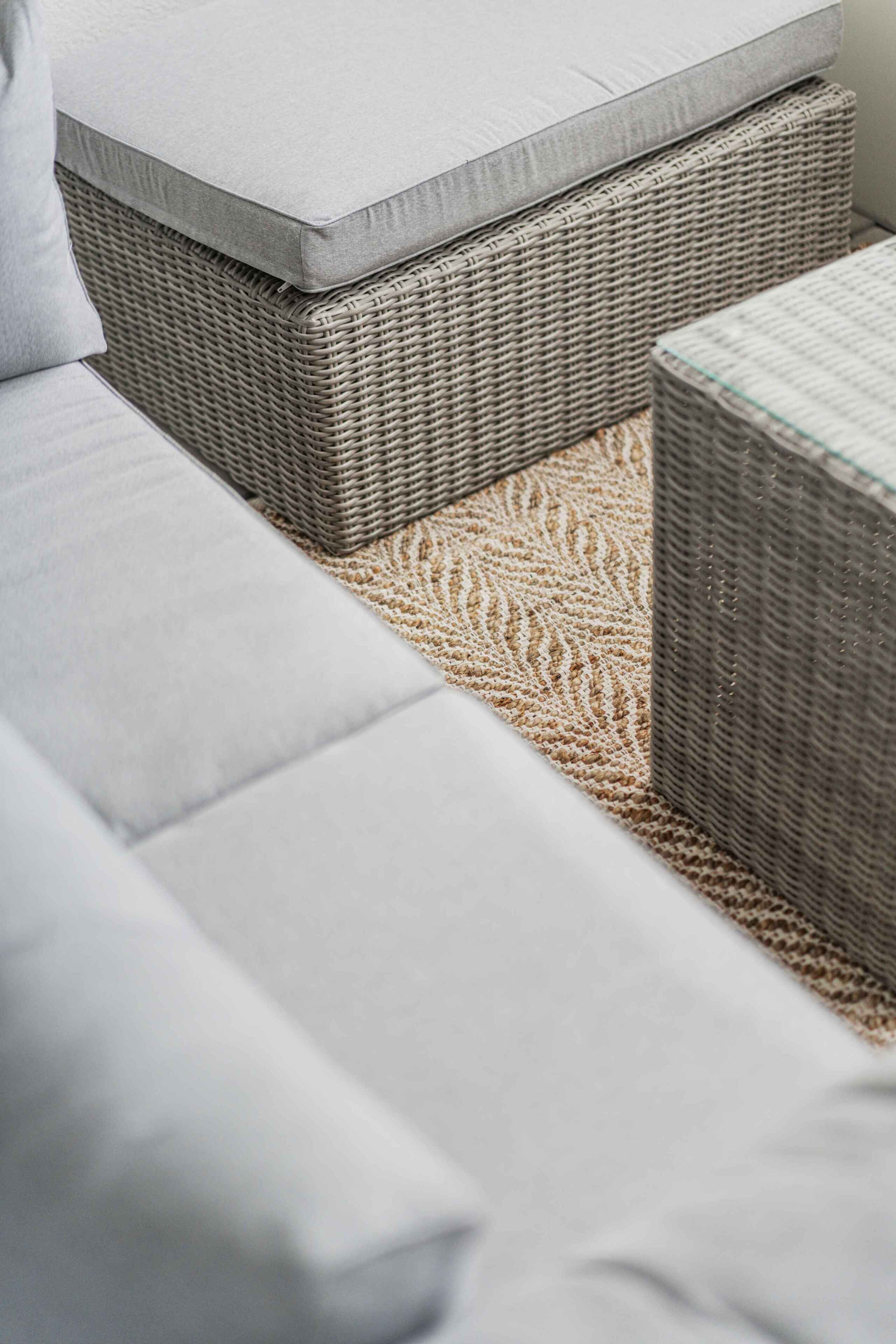 Ein Rattansofa mit Kissen, ein gewobener Hocker und ein strukturierter Teppich.