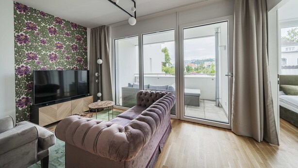 Una sala de estar moderna con un televisor de pantalla plana, un sofá, una mesa de centro y un ventanal corredero que da a un espacio exterior.