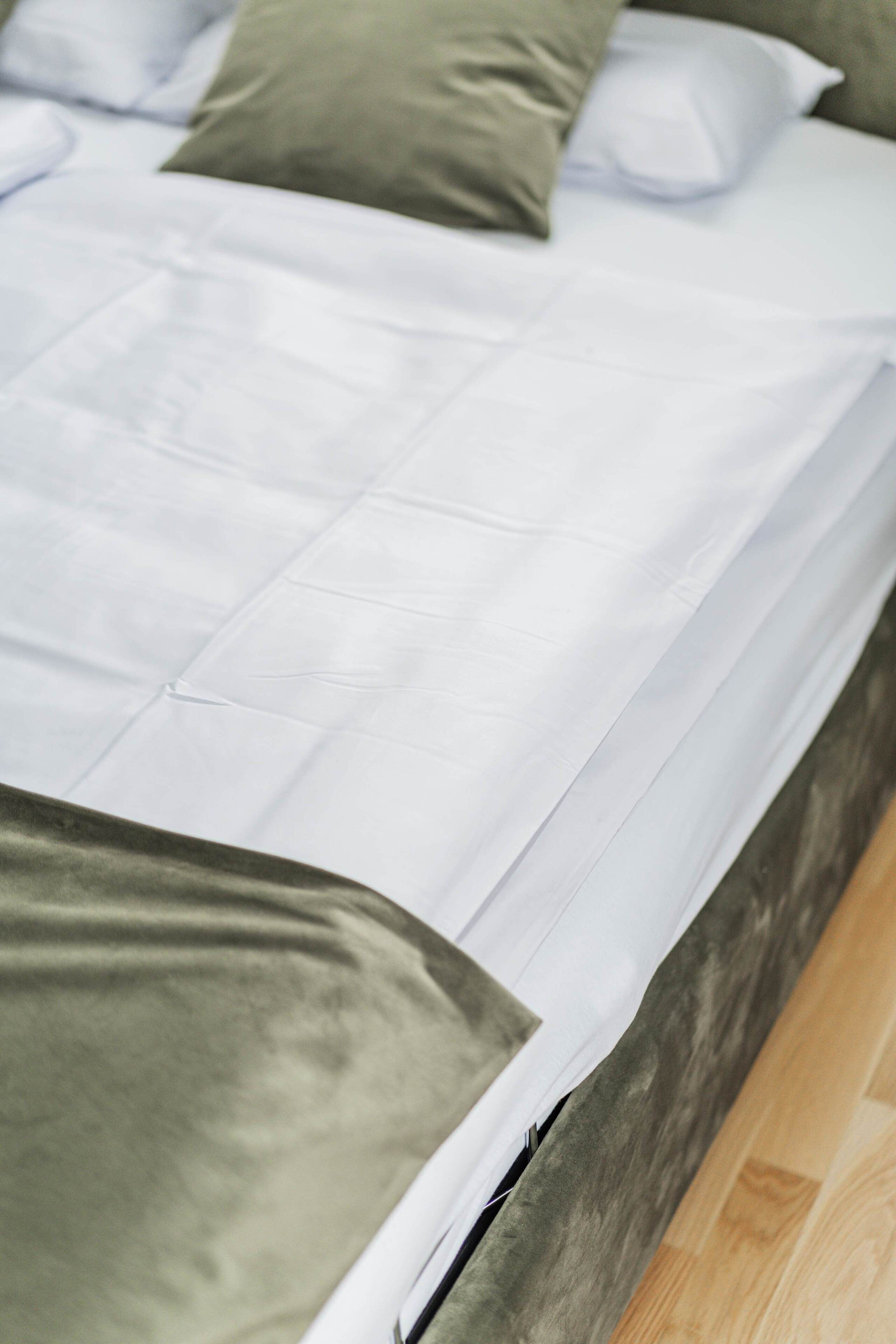 Una cama con ropa de cama blanca y una almohada verde.
